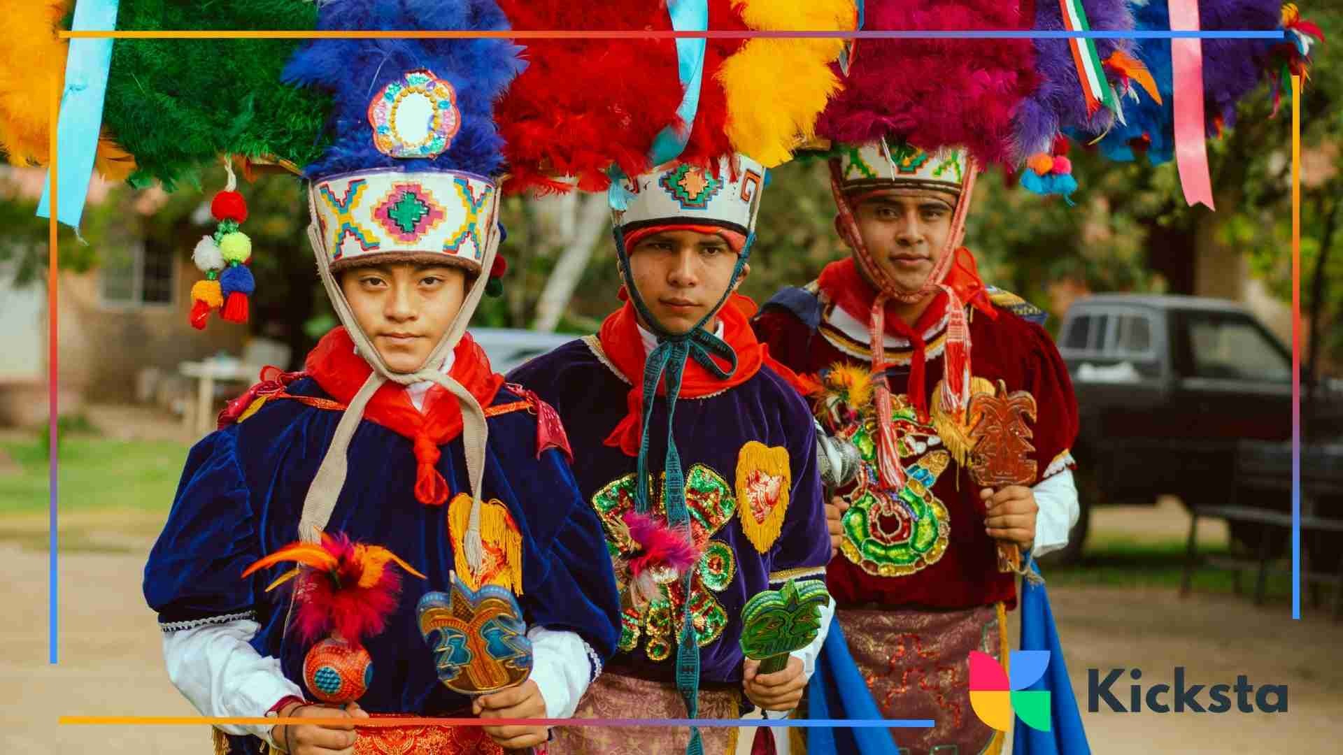 Three young men wearing colorful, heavily decorated traditional festival costumes with tall feathered headdresses and embroidered details, standing outdoors.