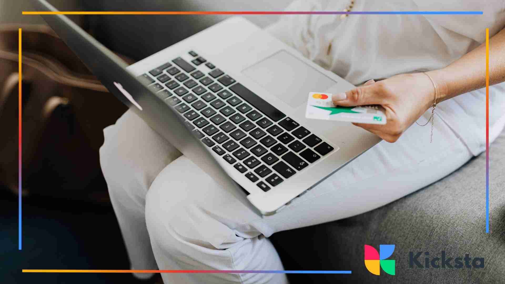 Person sitting on a couch with a laptop on their lap, holding a credit card while making an online purchase.