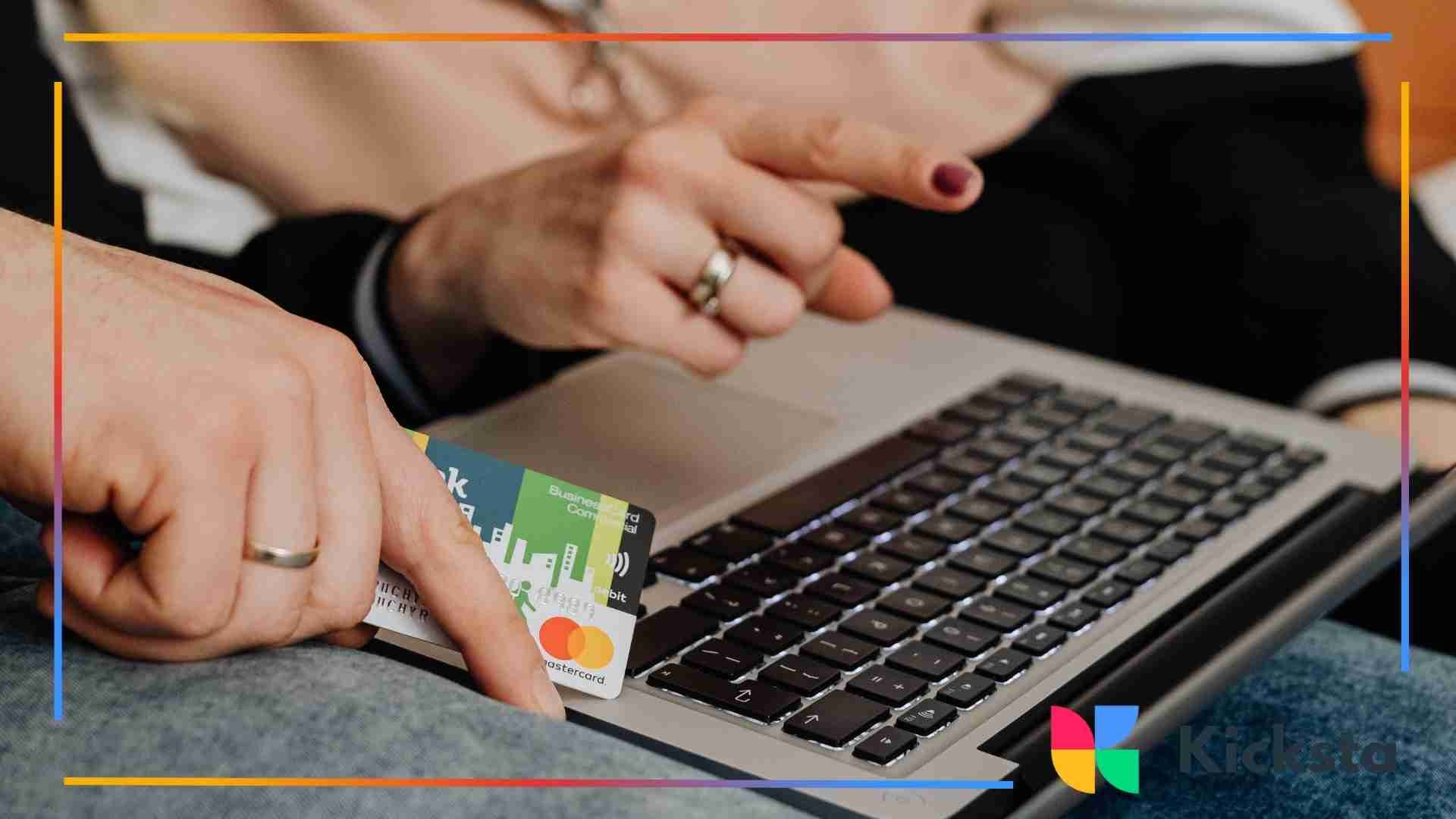 Close-up of two people using a laptop, with one person holding a credit card while the other points at the screen.