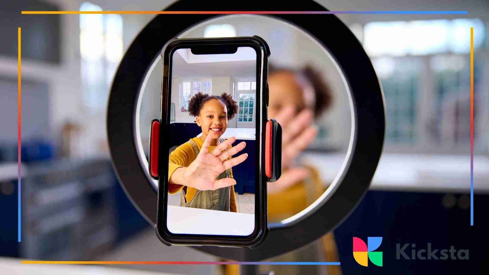 A person recording a video on a smartphone mounted in the center of a ring light, waving at the camera with an open hand.
