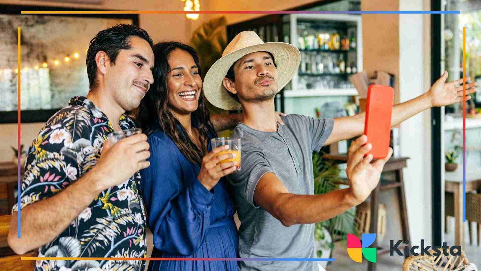 Three friends standing together in a restaurant, smiling and taking a group selfie with a smartphone while holding drinks.