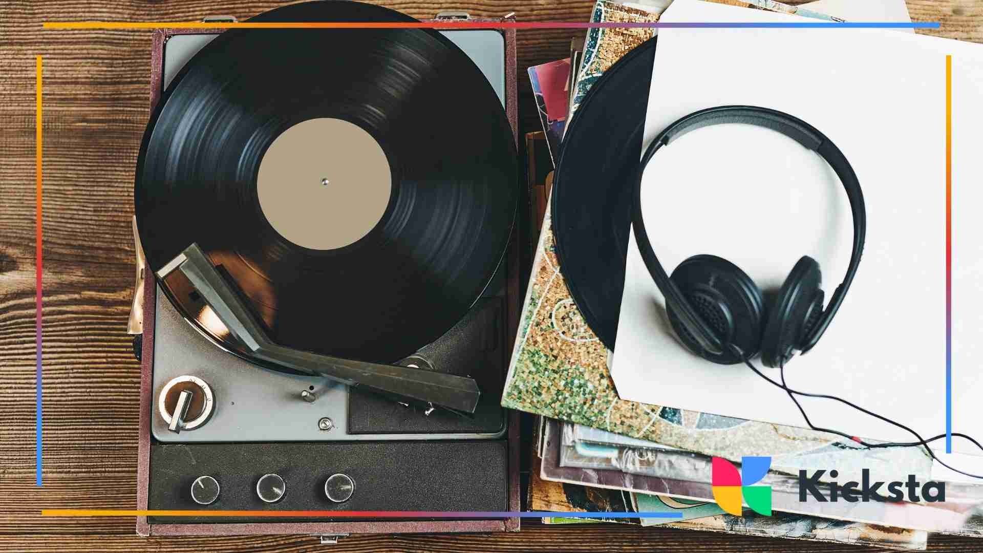 A vintage vinyl record spinning on a record player next to a pair of black headphones resting on a stack of album covers.