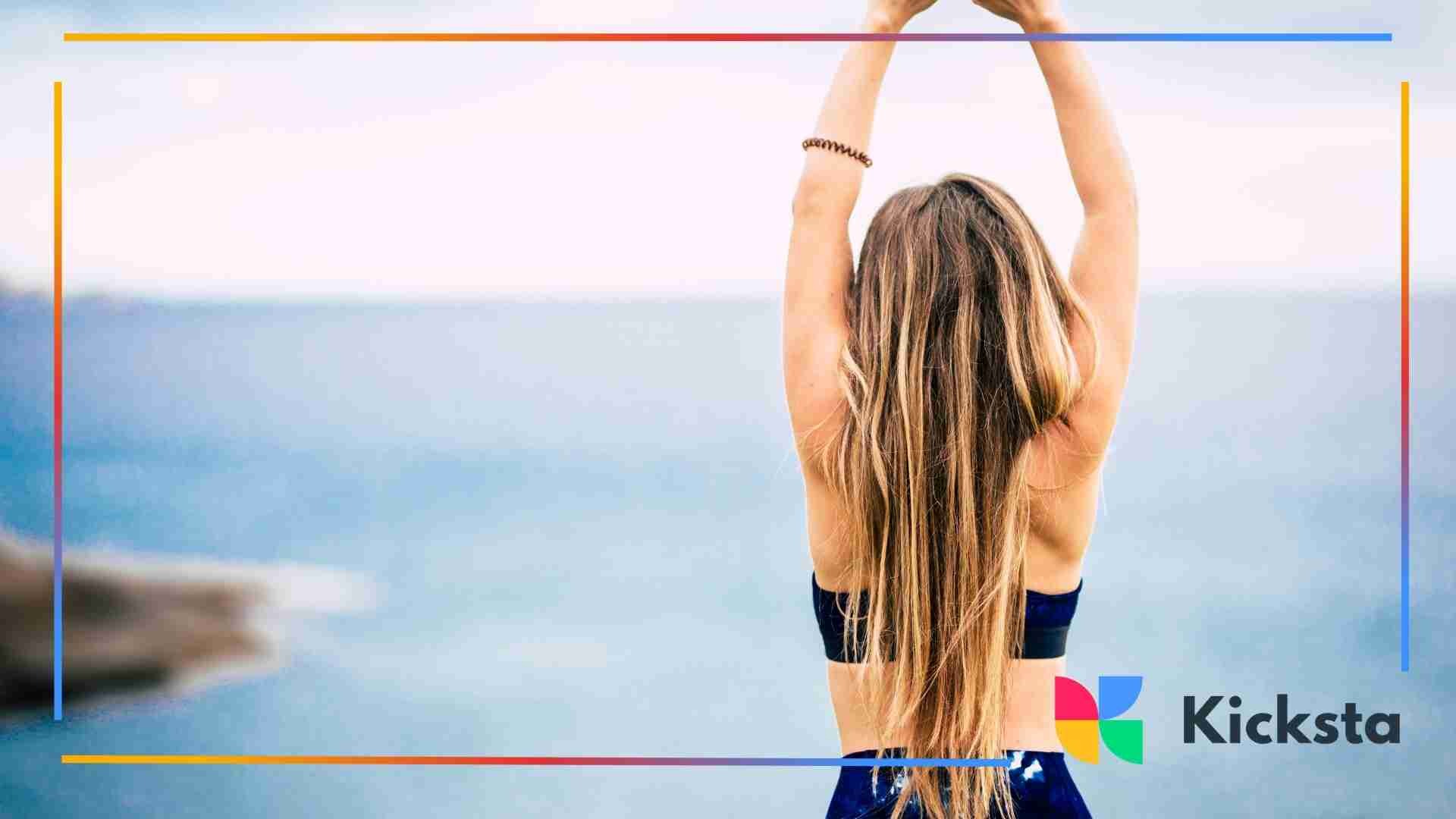 Woman stretching with her arms raised while standing near the ocean.
