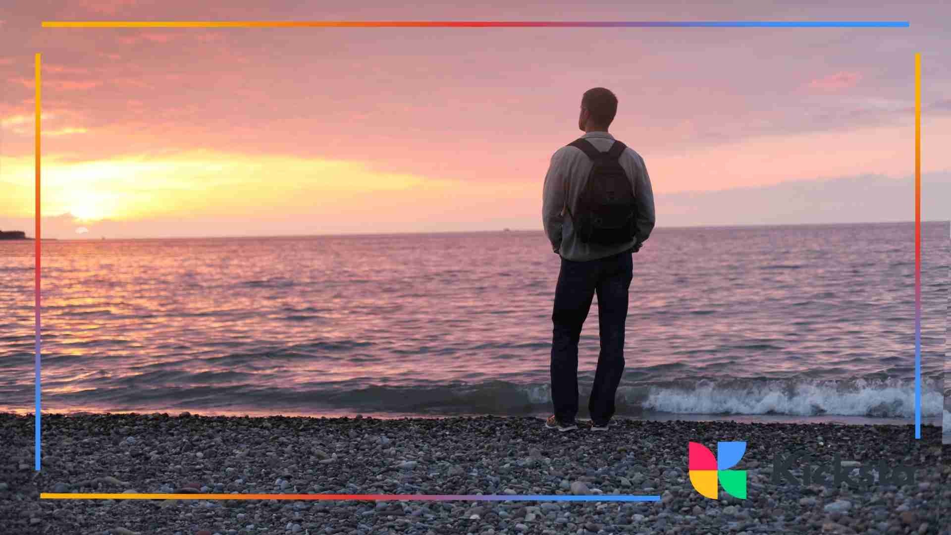 Man standing on a rocky beach watching the sunset over the ocean.