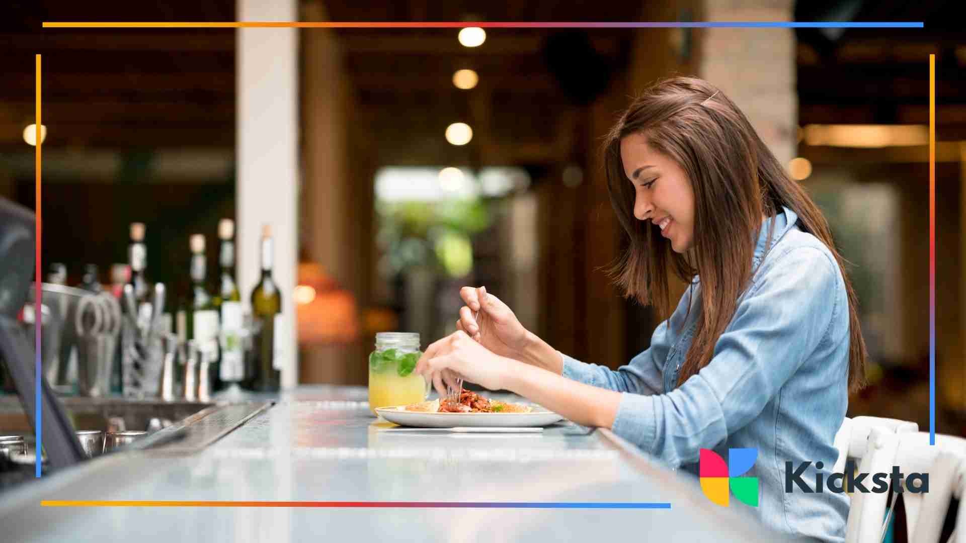 Woman sitting at a restaurant bar enjoying a meal with a drink beside her.