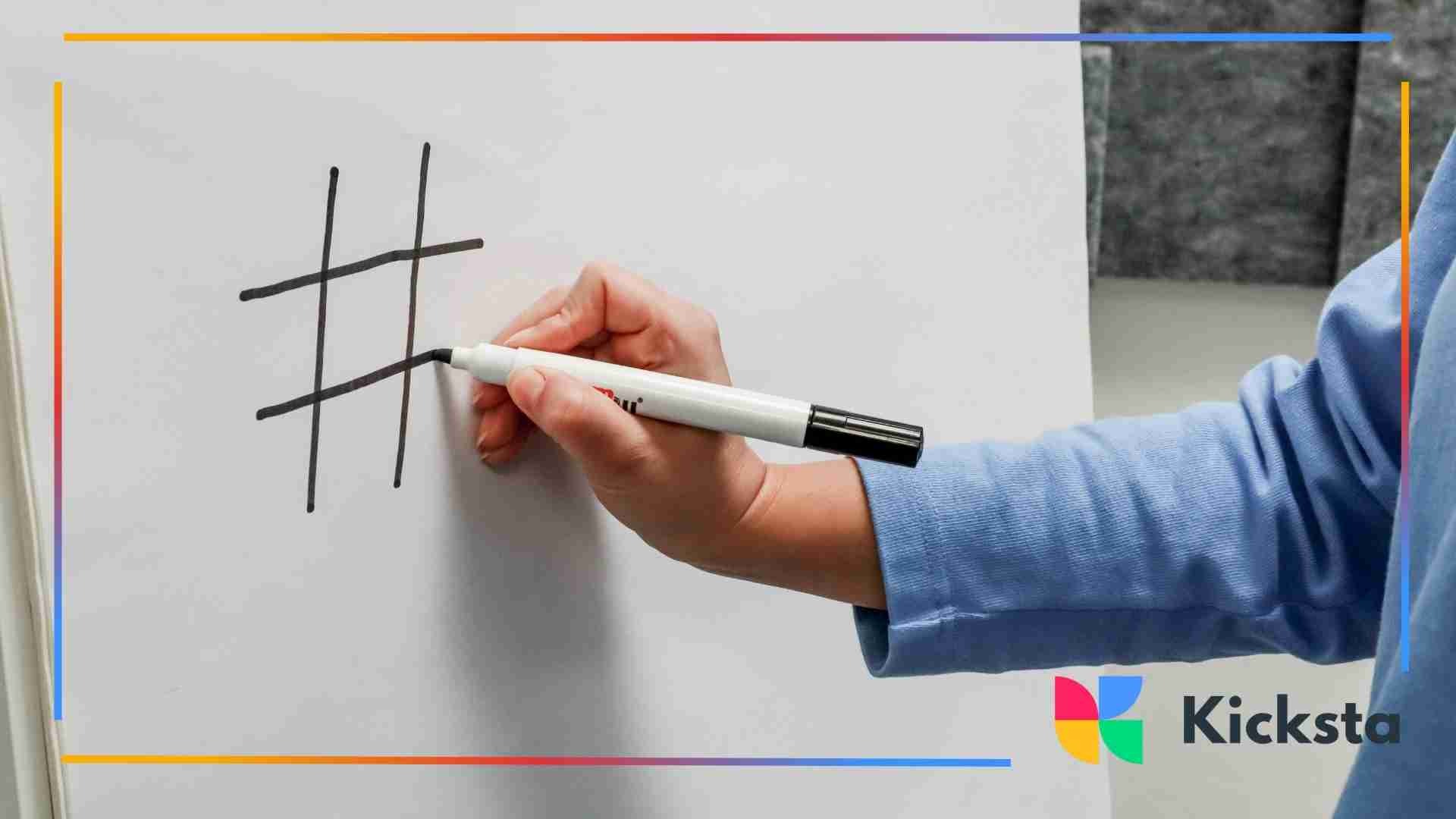 Hand drawing a large hashtag symbol on a whiteboard with a black marker.