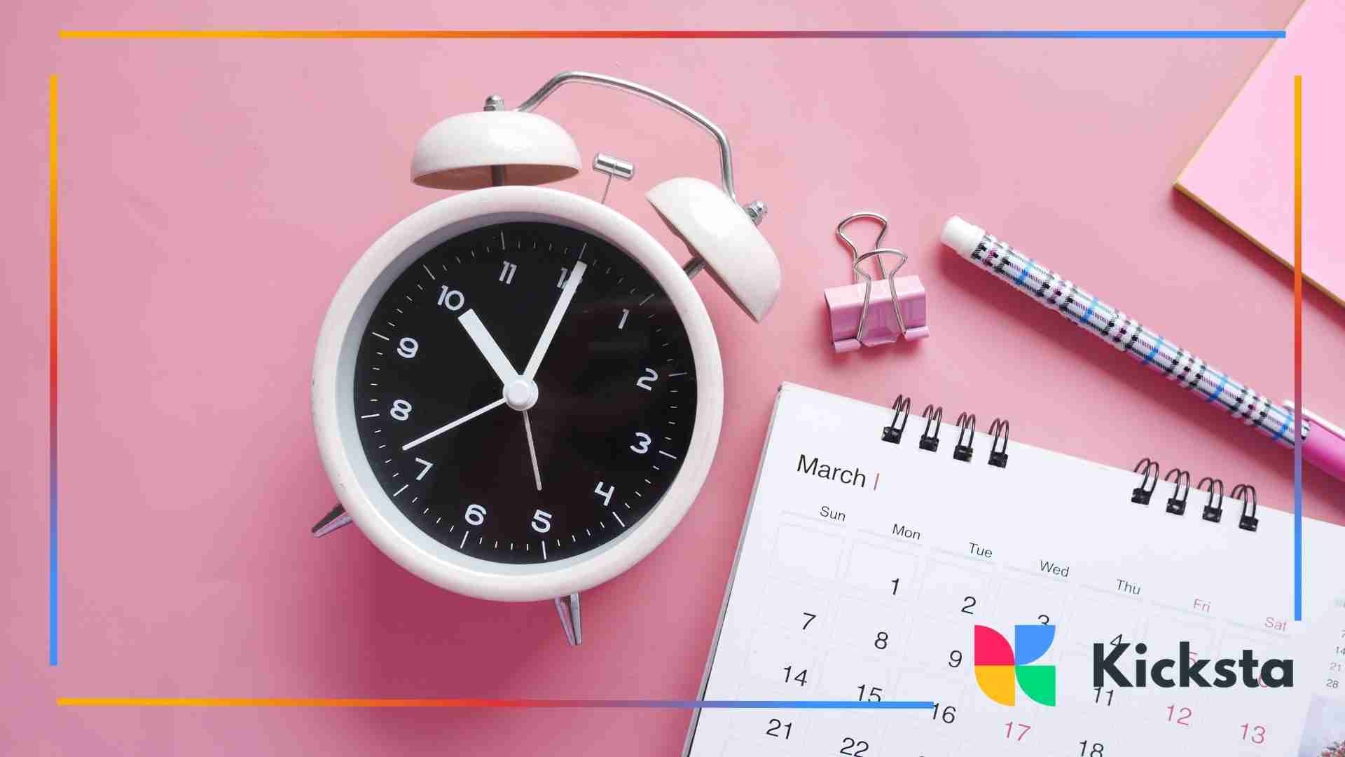 A white alarm clock, a March calendar, and office supplies arranged on a pink background.
