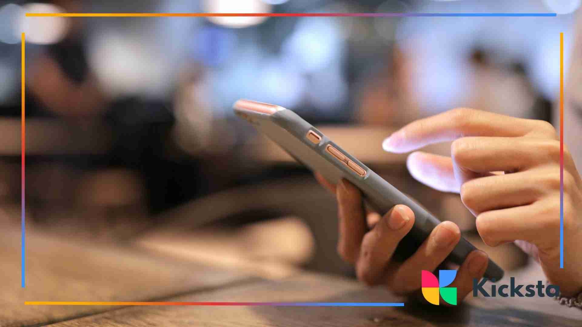 Close-up of someone holding a smartphone and tapping the screen in a blurred indoor setting.