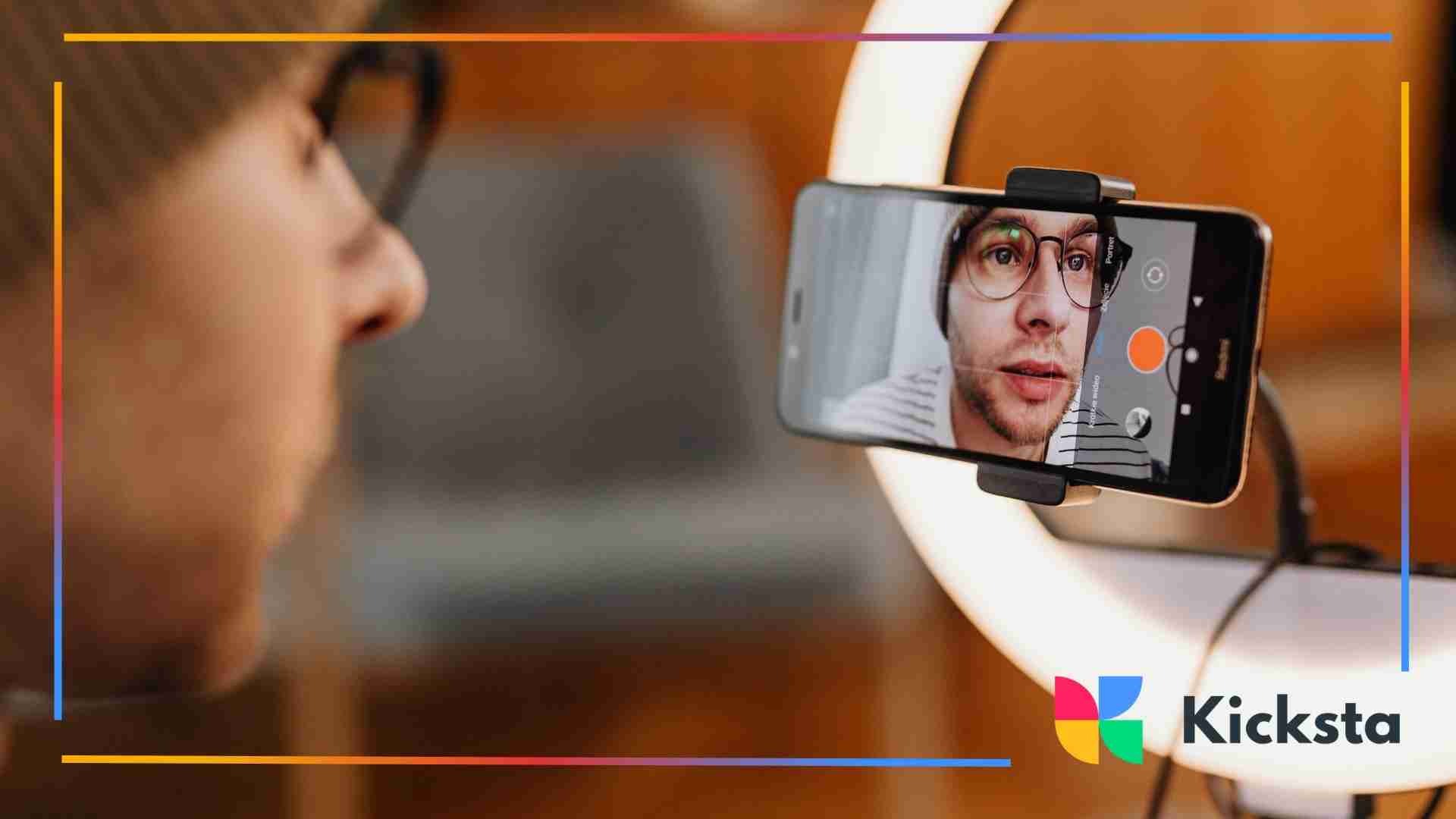 A person filming themselves with a smartphone mounted on a ring light, showing their face on the phone screen during recording.