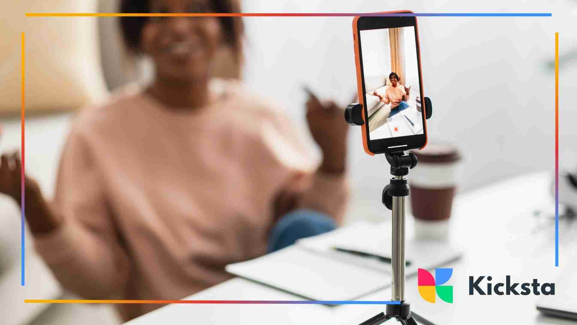 Smartphone recording a woman speaking enthusiastically while sitting at a desk with notebooks and a coffee cup.