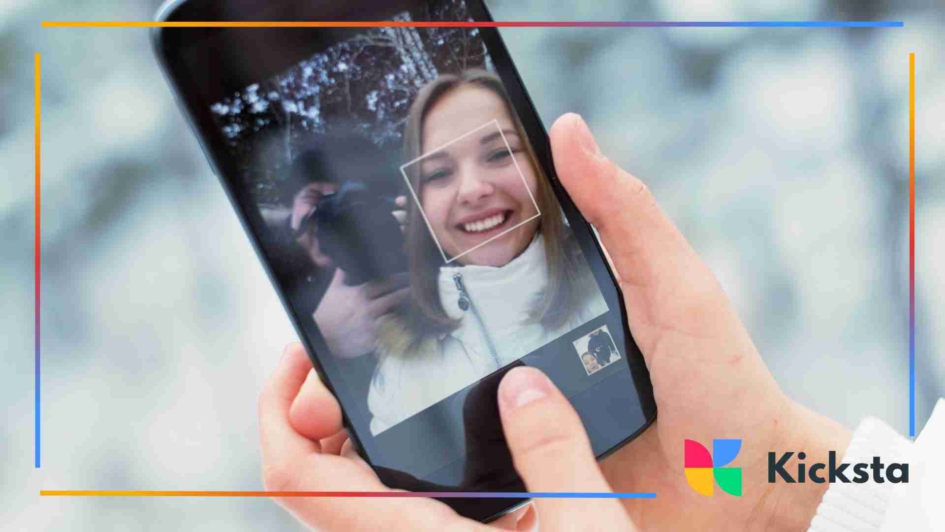 Close-up of a person holding a smartphone while taking a selfie with face-detection framing on screen.