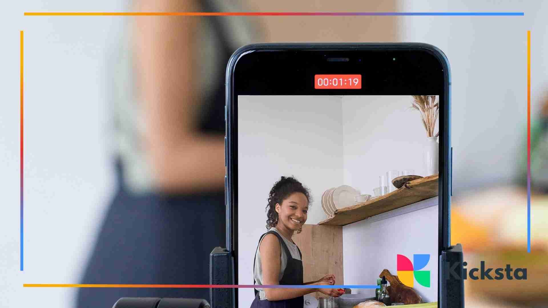 Phone screen showing a woman cooking in her kitchen as she records a video.