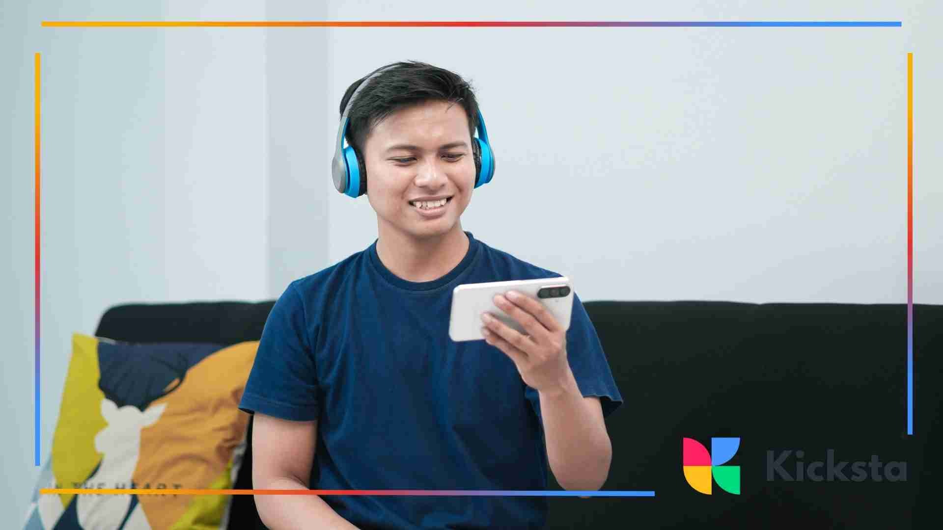 Person wearing blue headphones sitting on a couch and smiling while looking at a smartphone.