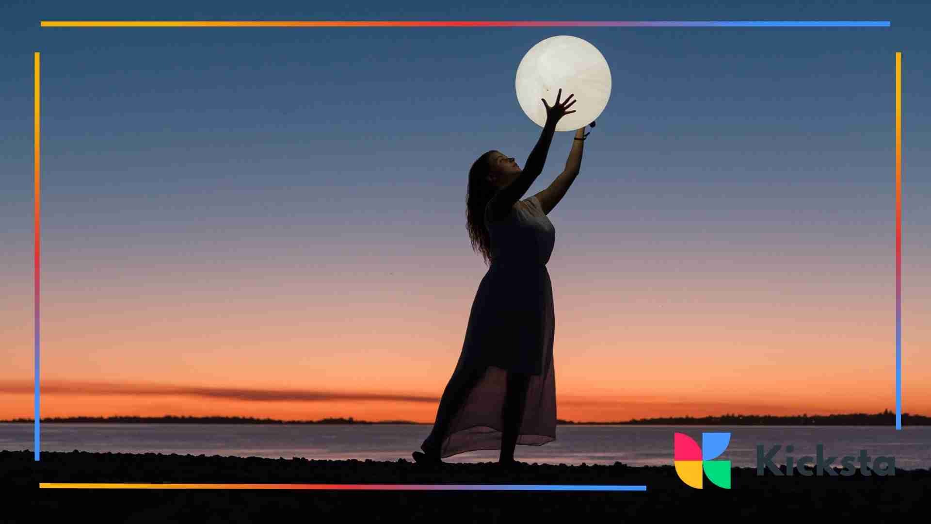 Silhouette of a woman at sunset holding a glowing sphere above her head.