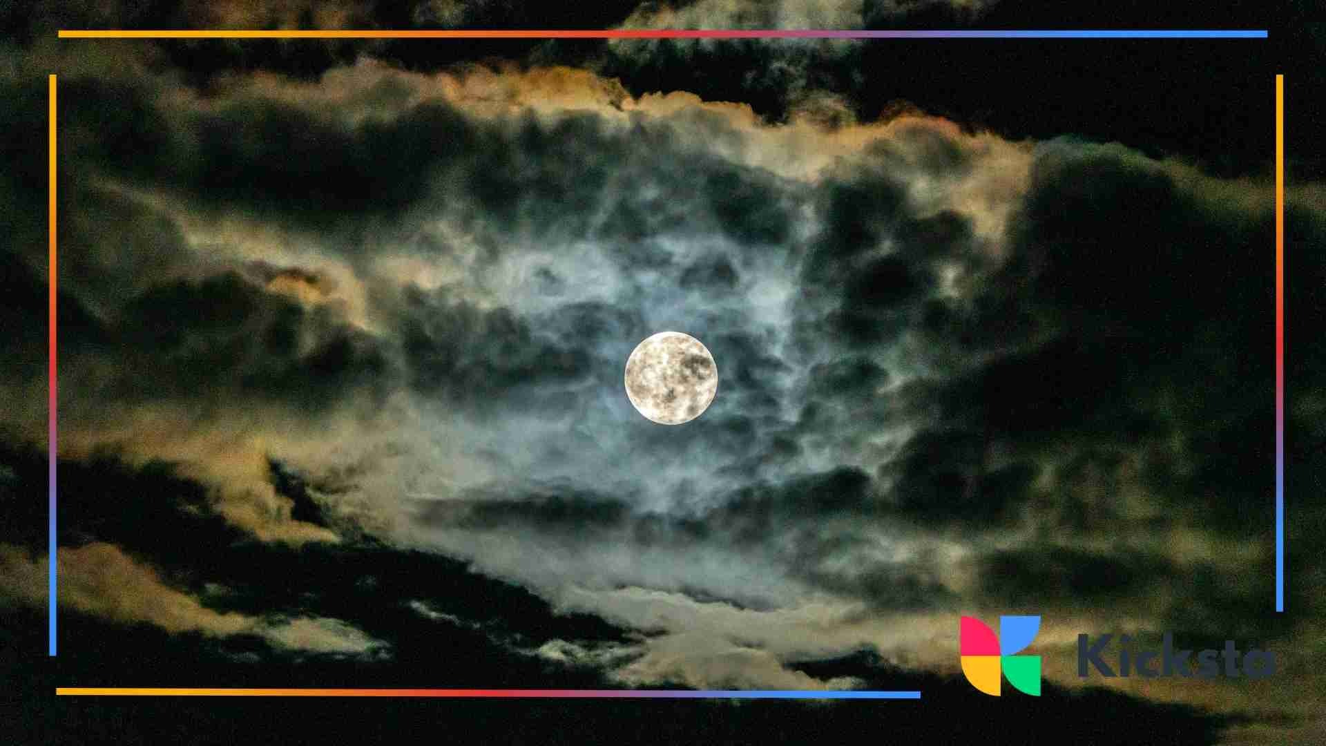 Full moon shining through dramatic, dark clouds at night.