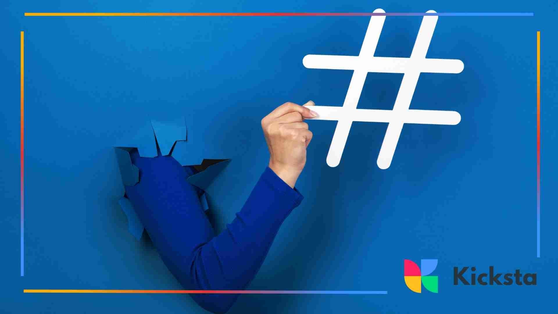 An arm breaking through a blue paper wall while holding a large white hashtag symbol.