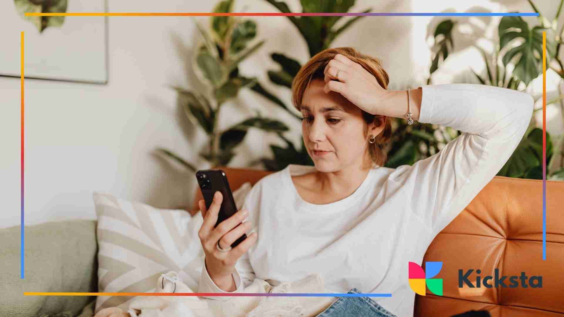 Woman sitting on a couch looking at her phone with a worried expression, surrounded by indoor plants.