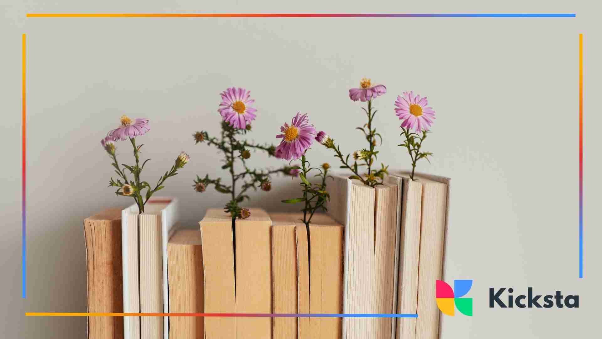 A row of vintage books with purple daisy-like flowers growing between the pages, creating a whimsical aesthetic.