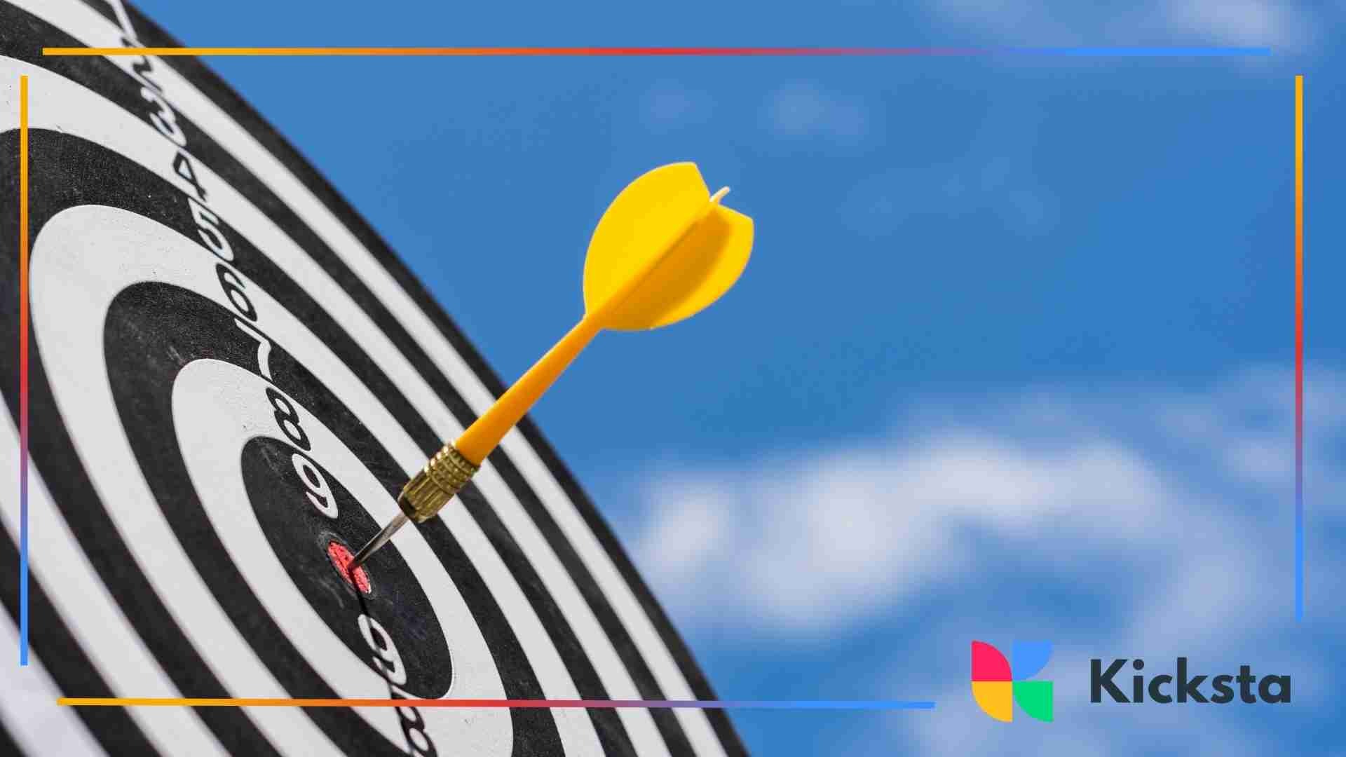 A yellow dart hitting the center of a black-and-white dartboard against a bright blue sky.