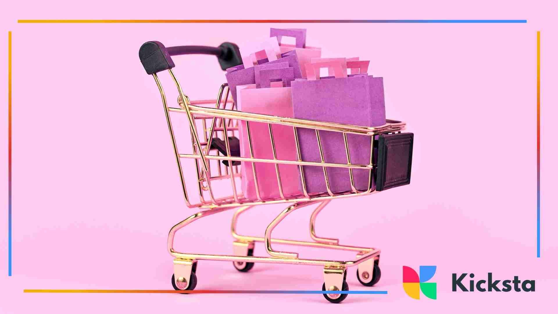 A small gold shopping cart filled with purple and pink paper shopping bags on a pastel pink background.