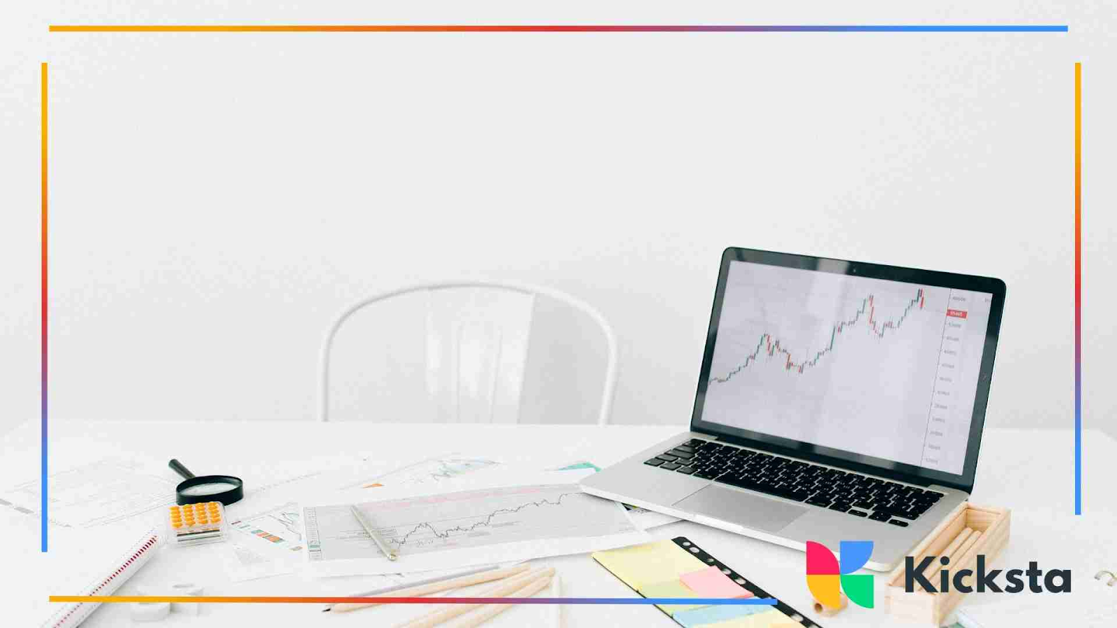 A laptop displaying a rising line graph sits on a cluttered white desk with papers, charts, a ruler, and a calculator.