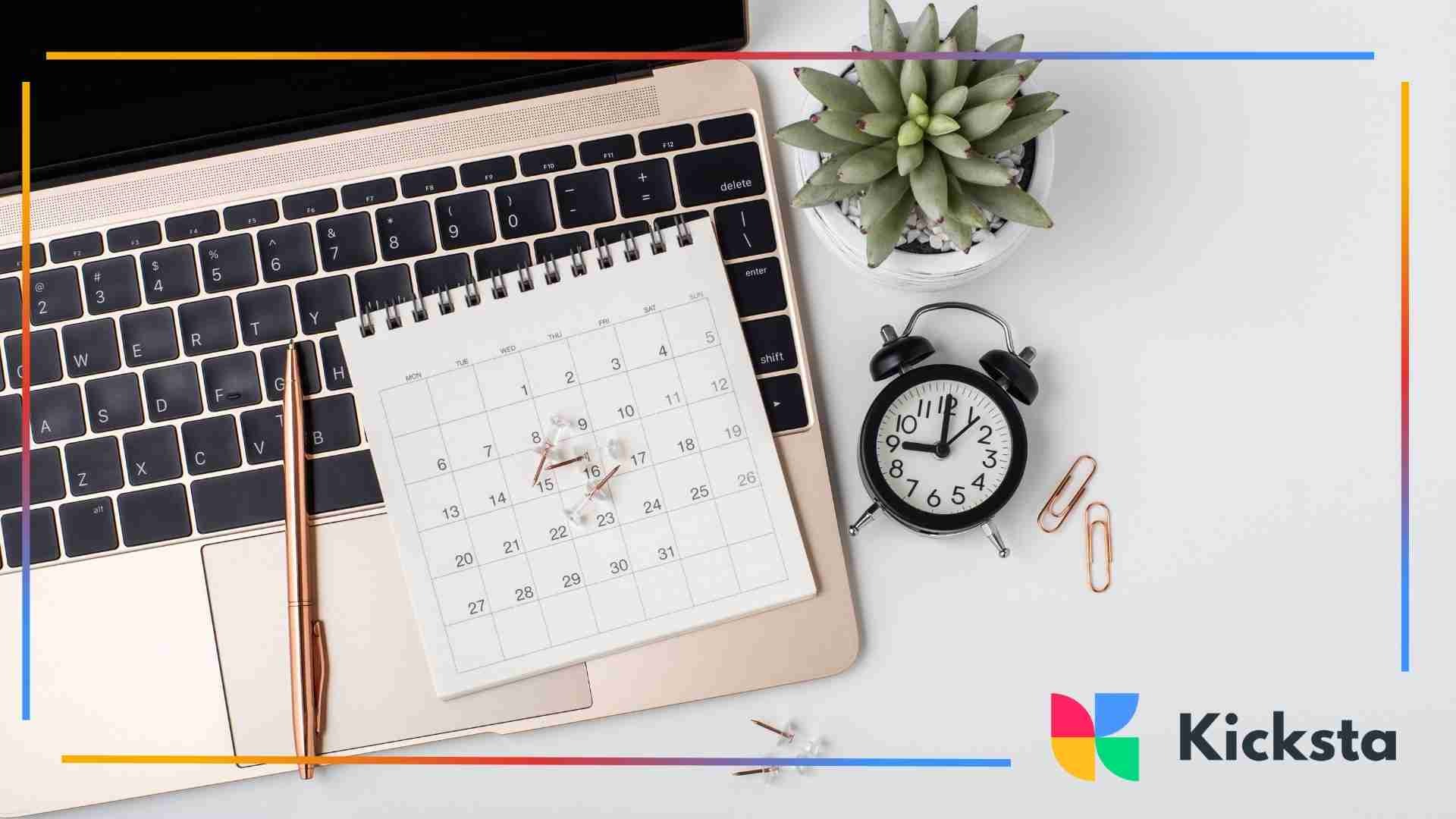 Top-down view of a laptop keyboard with a small desk calendar, clock, succulent plant, and office supplies arranged neatly.