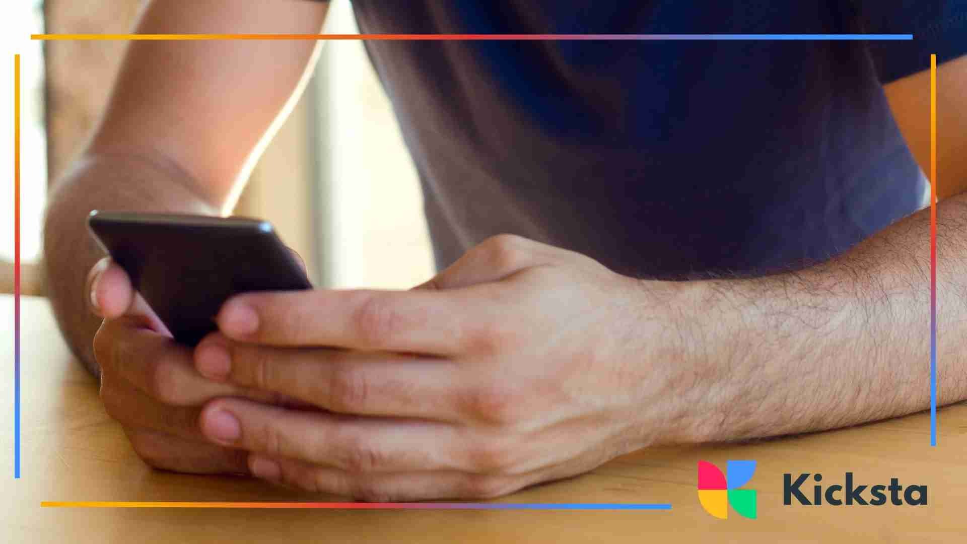 Close-up of a person using a smartphone with both hands while sitting at a wooden table.