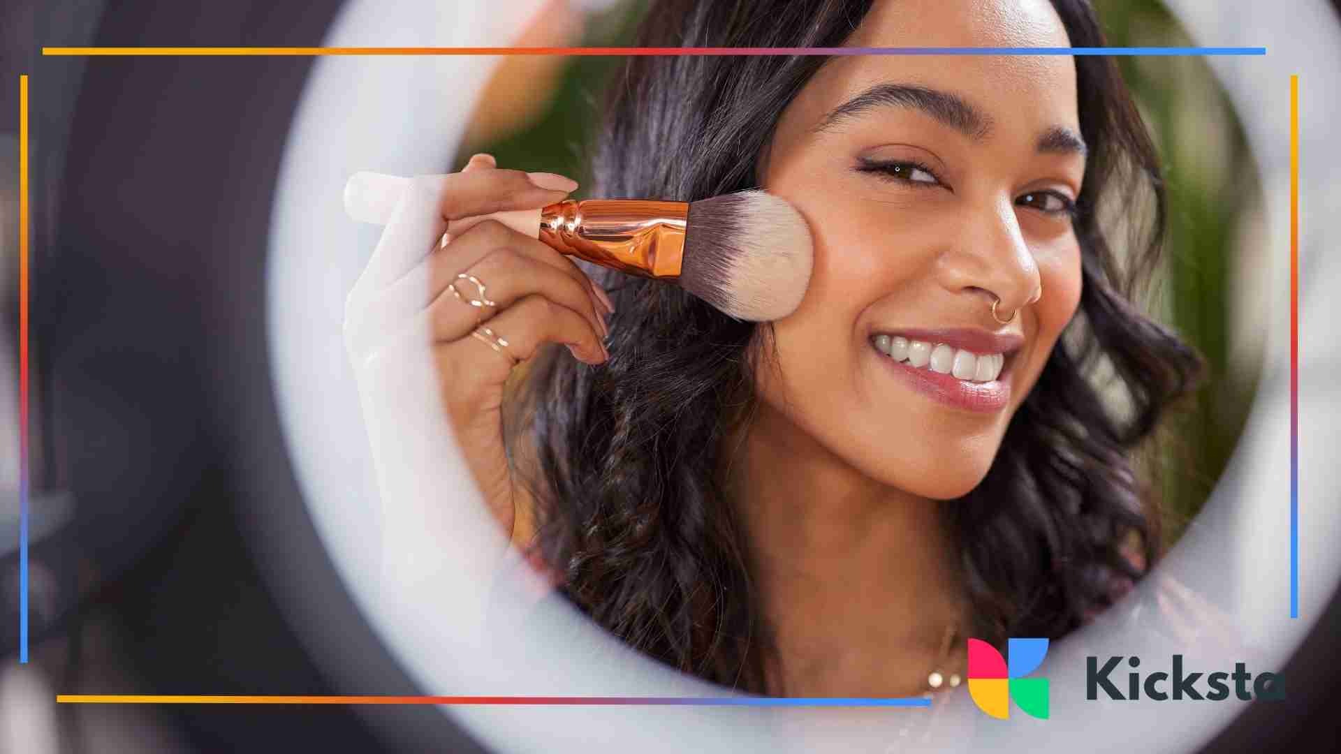 A woman smiling into a ring light while applying makeup with a large brush on her cheek.