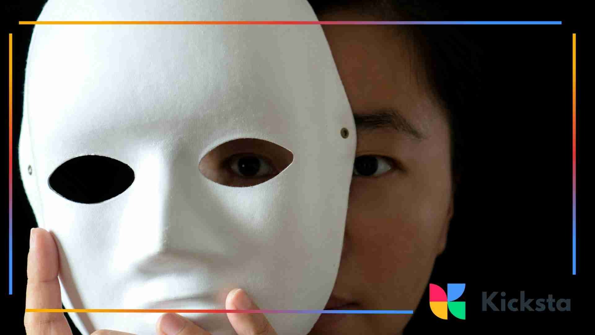 A person holding a white mask in front of their face, revealing only one eye visible through the mask’s opening.