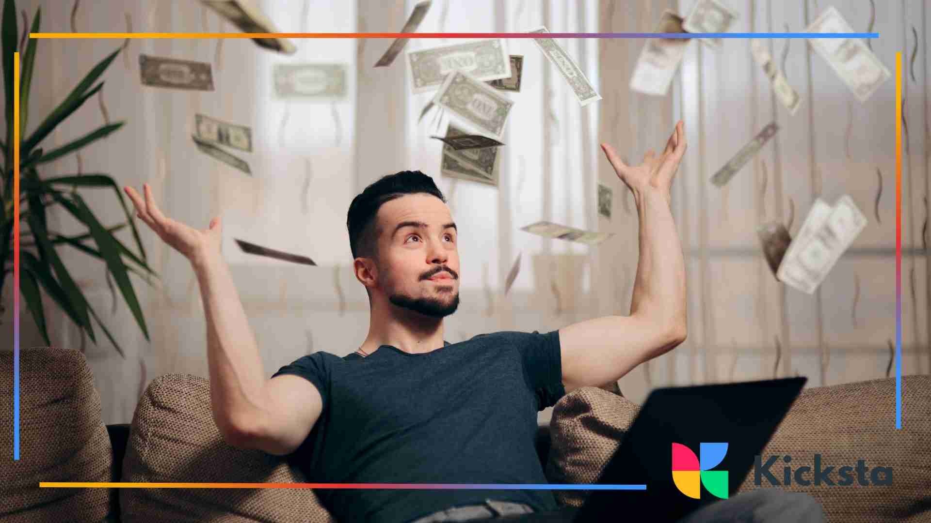 Man sitting on a couch tossing dollar bills into the air with a laptop in front of him, expressing excitement about earning money online.