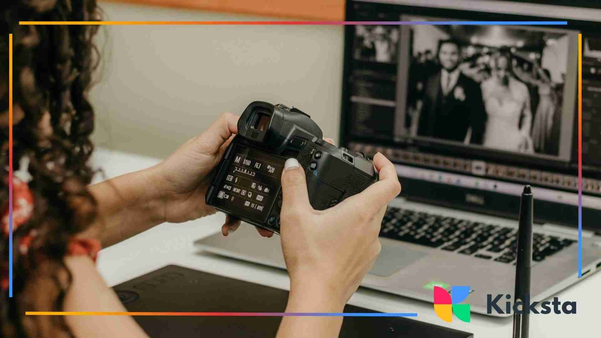 Person holding a digital camera while reviewing settings and images, with photo-editing software open on a nearby laptop.