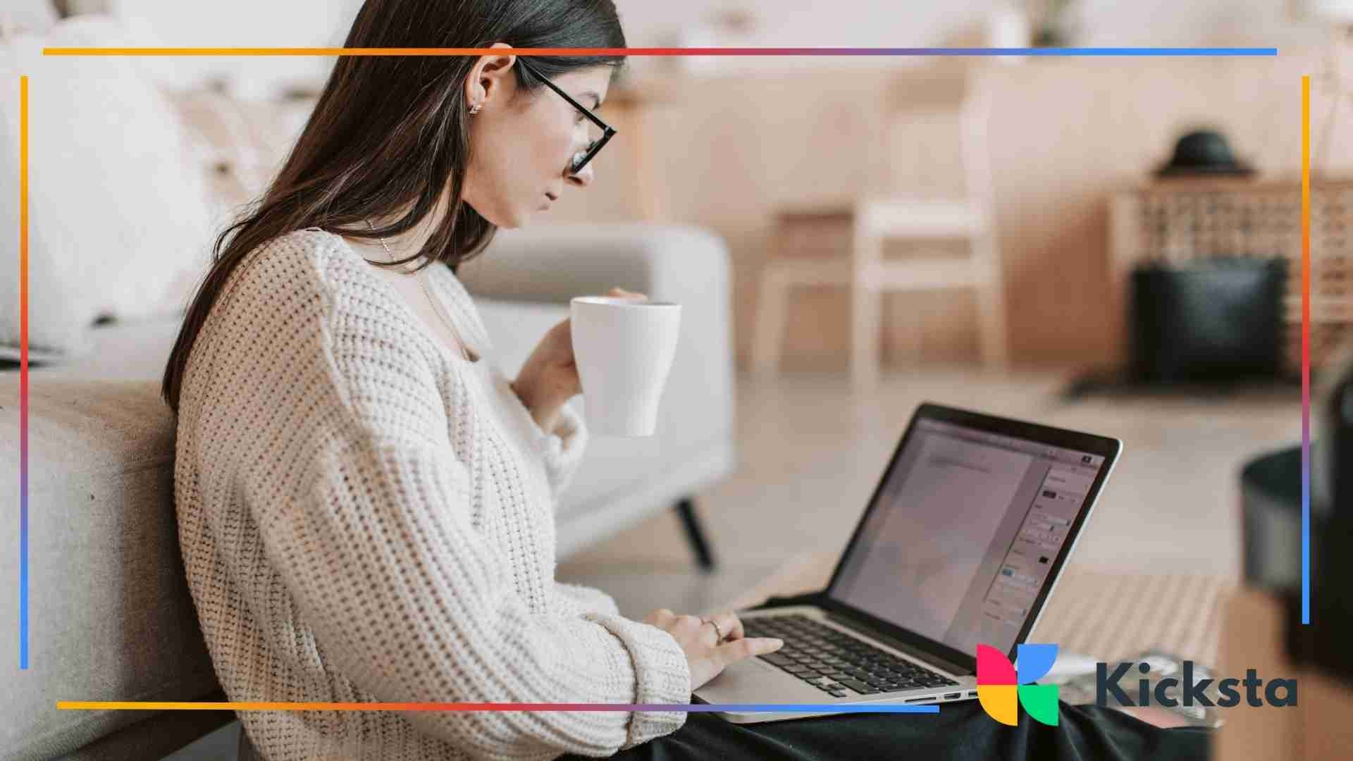 Woman in glasses working on her laptop while holding a cup of coffee in a cozy living room setting.