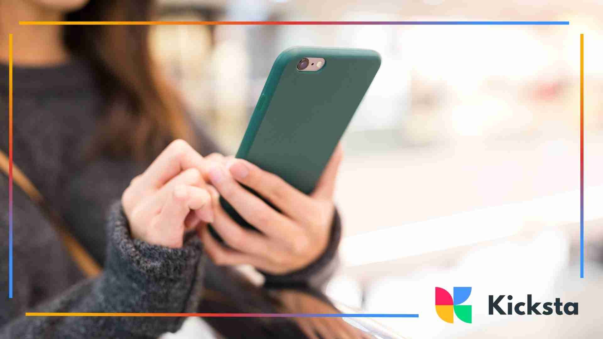 Woman holding a smartphone with both hands while standing indoors.