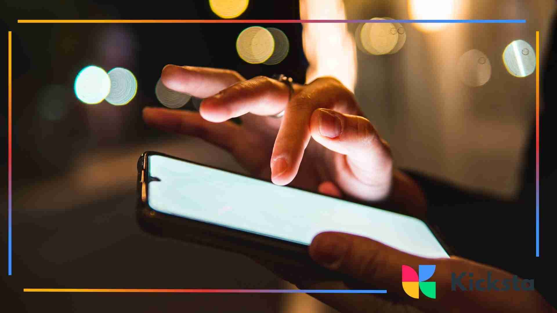 Close-up of a person using a smartphone at night with blurred city lights in the background.