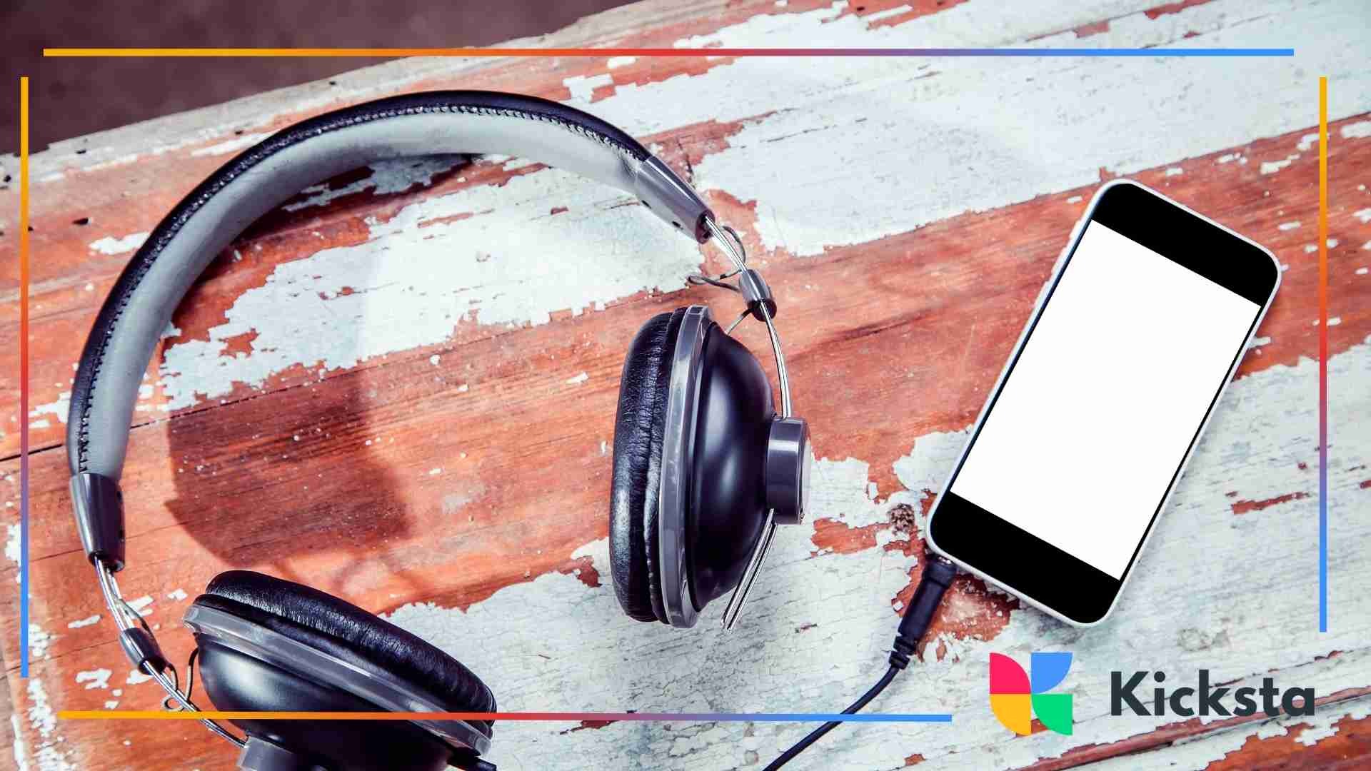 Over-ear headphones plugged into a smartphone resting on a distressed wooden surface.