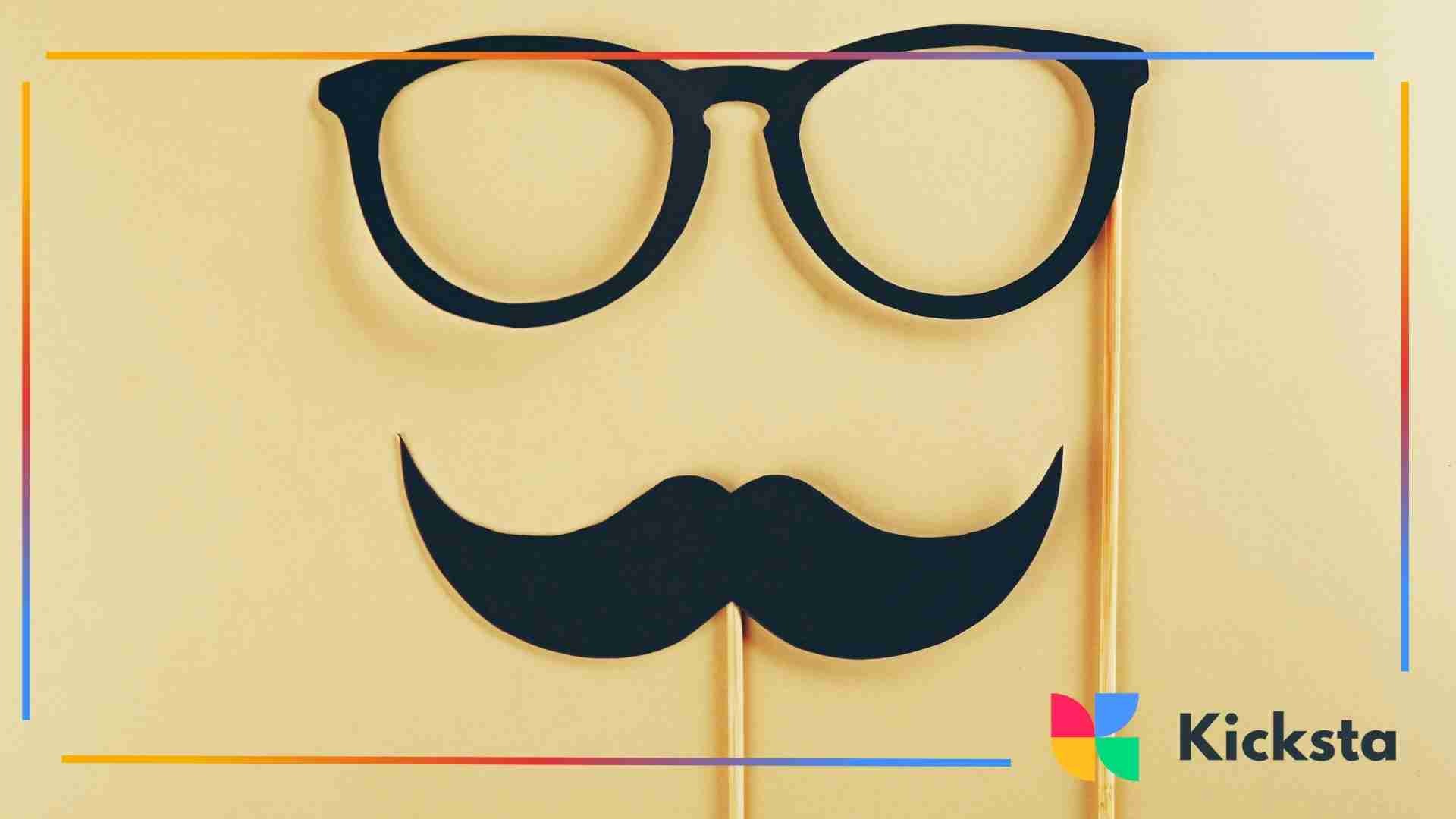 Paper cutouts of black glasses and a mustache on sticks against a beige background, resembling a playful disguise prop setup.