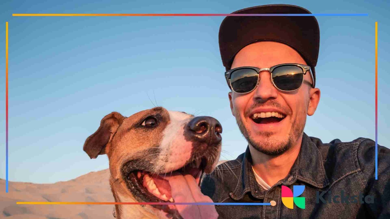 A smiling man wearing sunglasses takes a selfie with his happy dog in an outdoor setting under a bright blue sky.