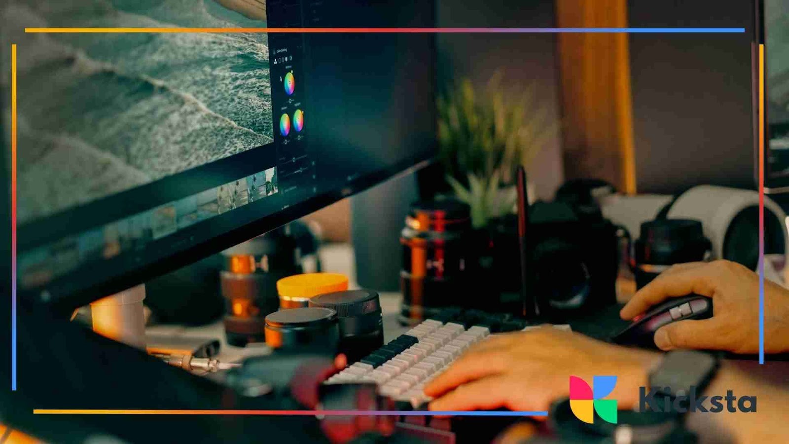 A close-up of a computer workstation showing a large monitor with video editing software open, surrounded by camera lenses and equipment, with a person using a mouse and keyboard.