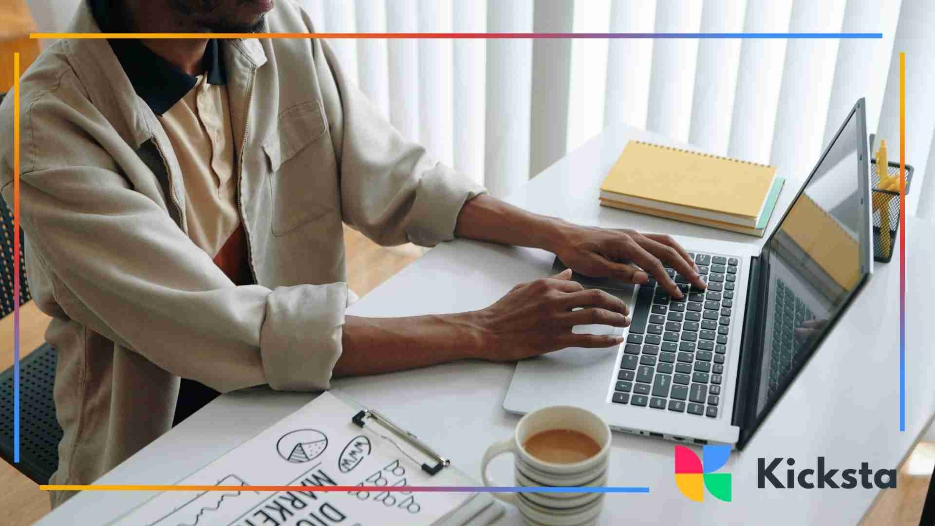 Person typing on a laptop at a desk with notebooks, coffee, and digital marketing sketches beside them.