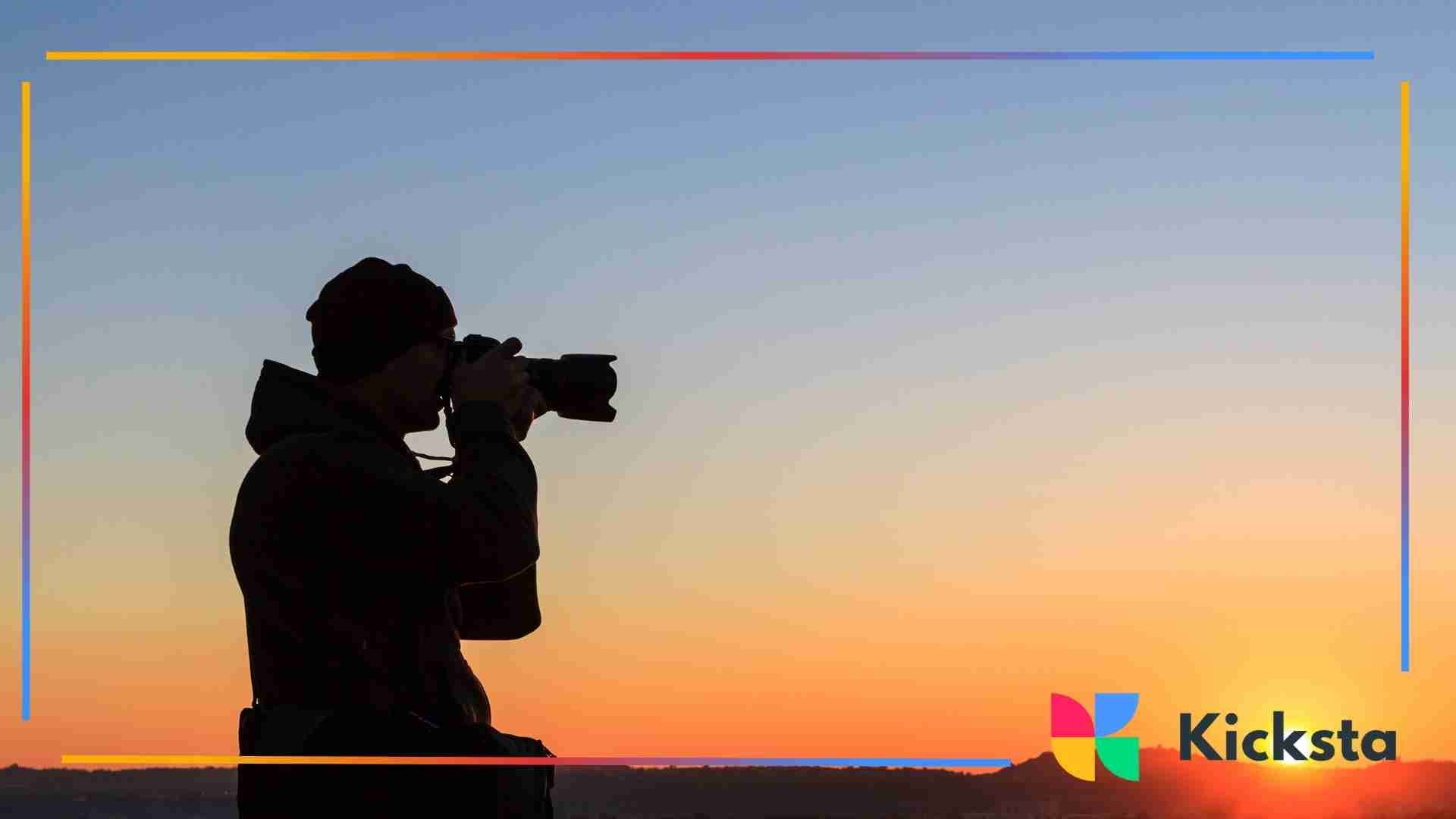 A silhouette of a photographer holding a camera and taking a picture against a colorful sunset sky.