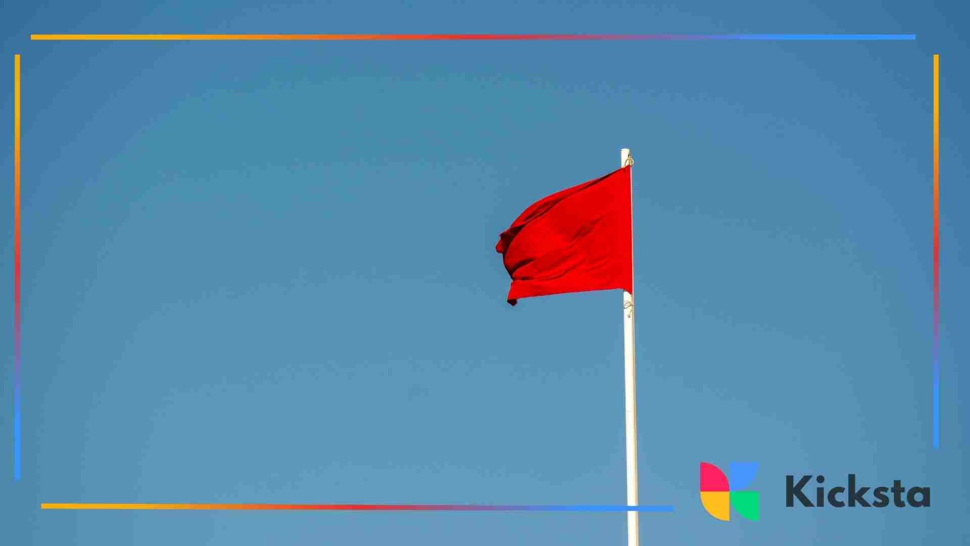 A red flag waving on a tall white pole against a clear blue sky, symbolizing warning signs.