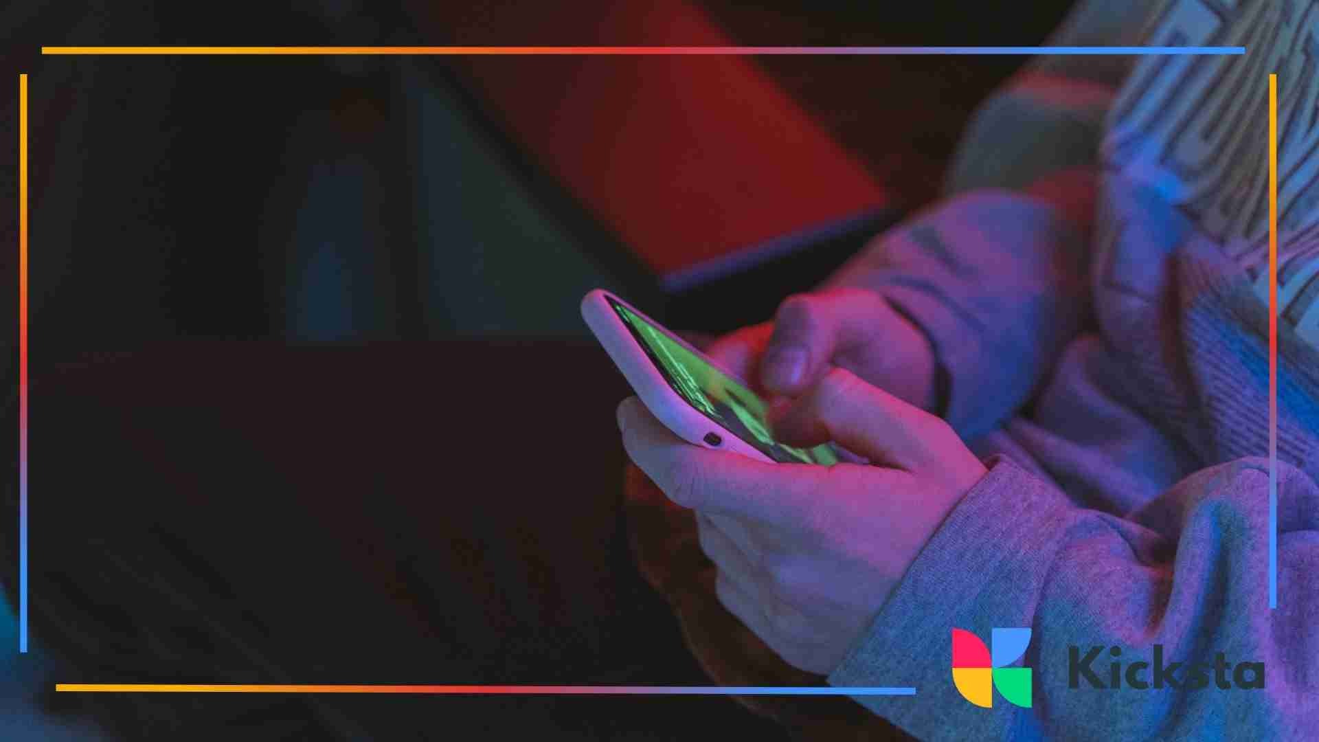 Close-up of a person using a smartphone under colorful neon lighting.
