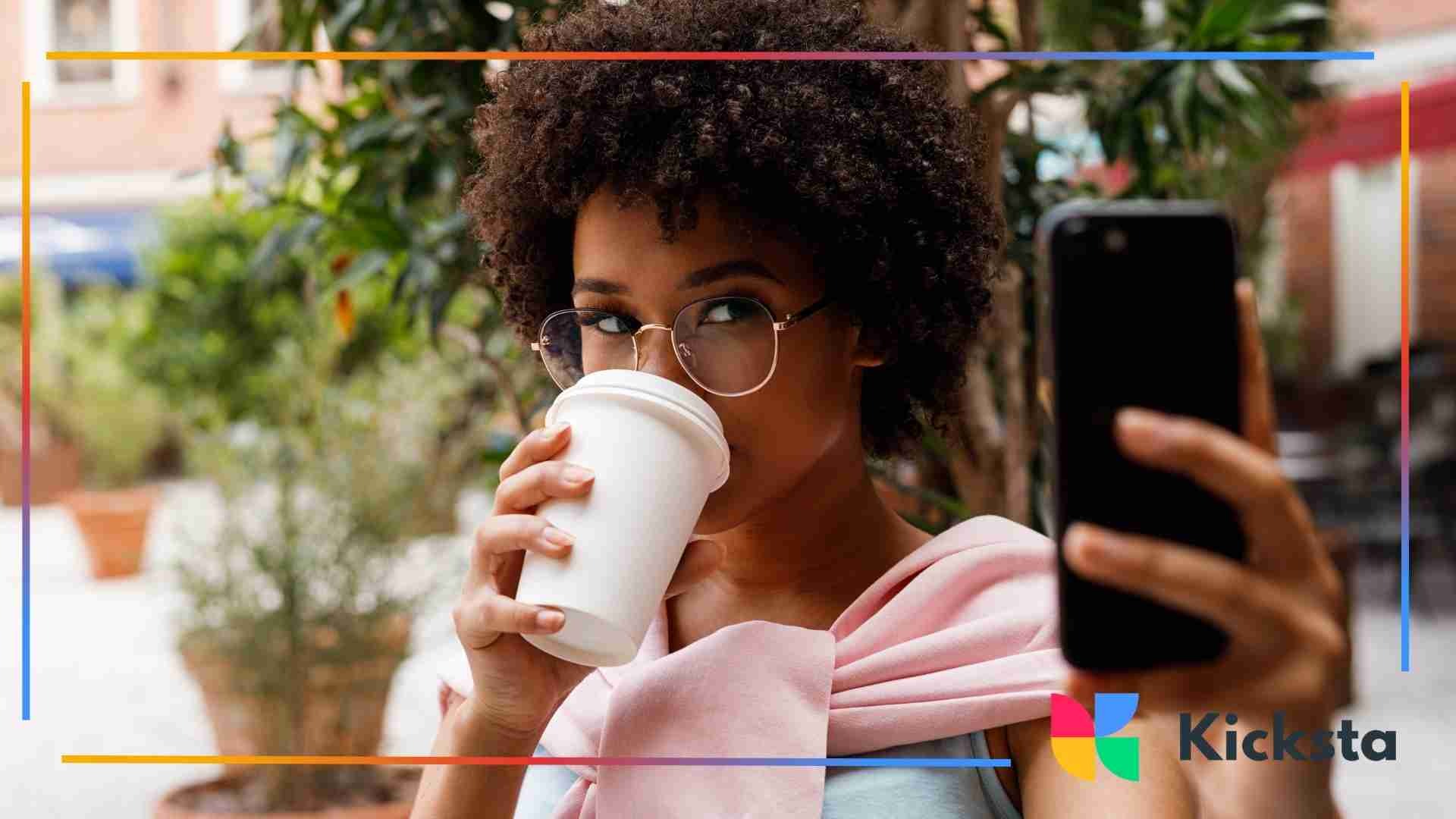 Woman drinking from a takeaway coffee cup while taking a selfie outdoors.
