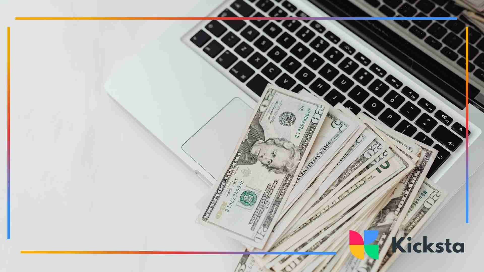 A pile of U.S. dollar bills spread across the keyboard of an open laptop on a white surface.