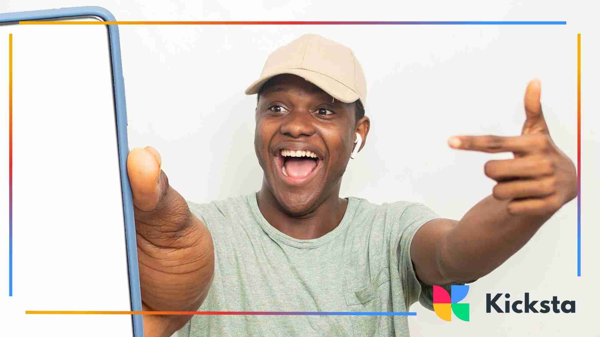 Smiling man wearing a cap and earbuds pointing excitedly at a smartphone with a blank screen.