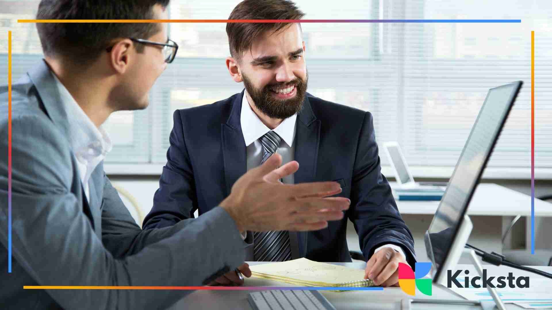 Two professionals discussing data and smiling while reviewing information on a desktop computer.