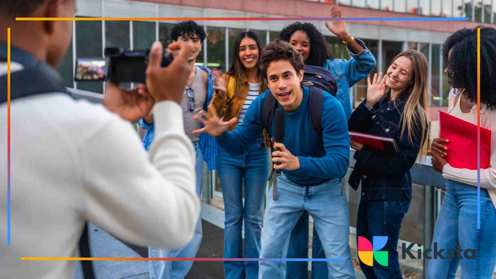 Group of young adults smiling and waving while being recorded on a handheld camera outdoors.