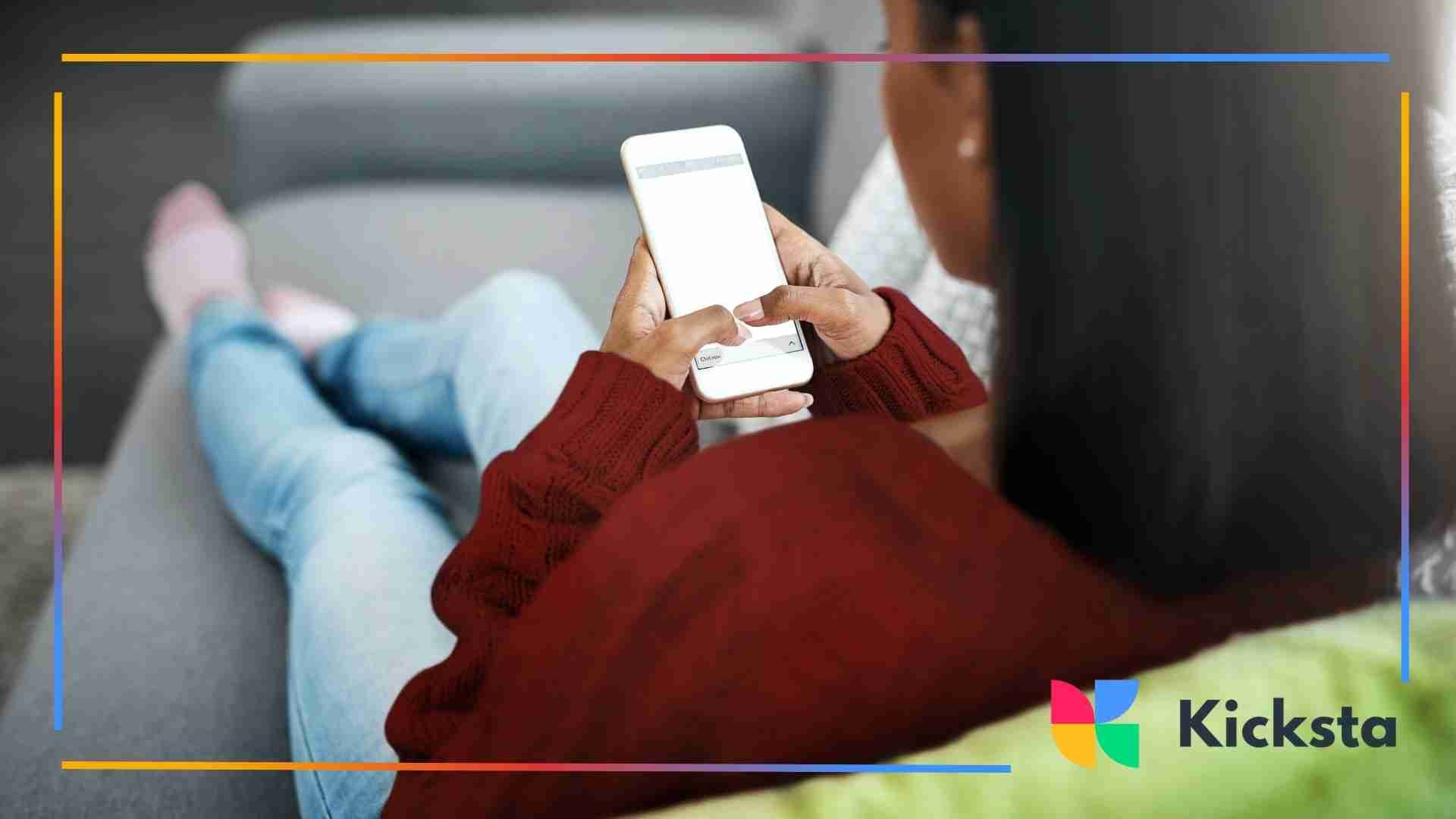 A woman wearing a maroon sweater sitting on a couch and typing on her smartphone, with her legs crossed and a cozy, relaxed atmosphere.