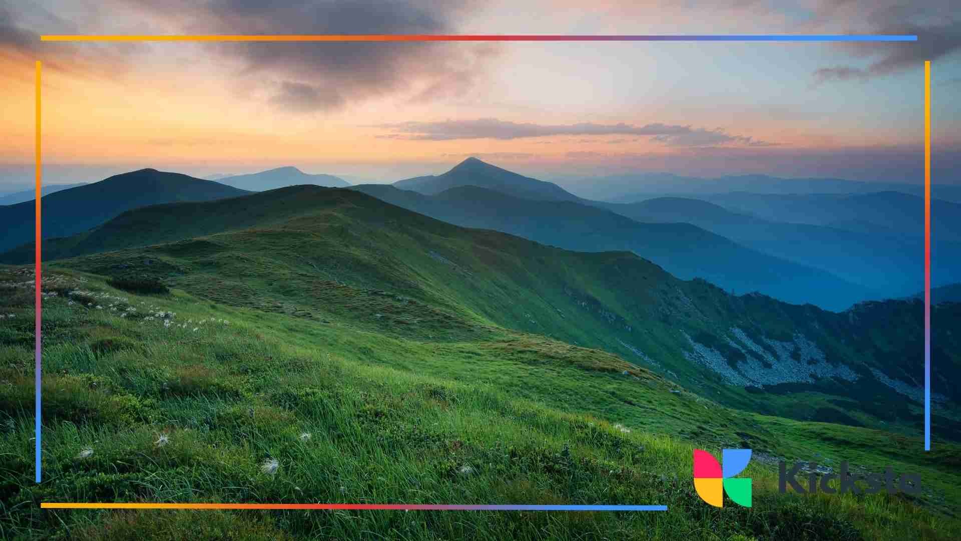 Soft evening light illuminating rolling mountain ridges covered in green grass beneath a colorful sunset sky.
