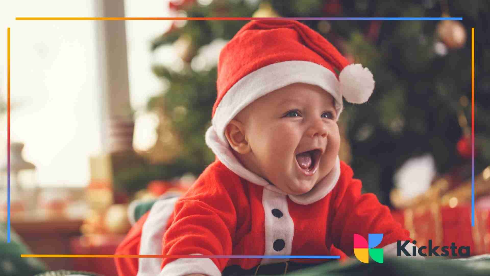 Smiling baby wearing a red Santa outfit and hat, laughing in front of a decorated Christmas tree.